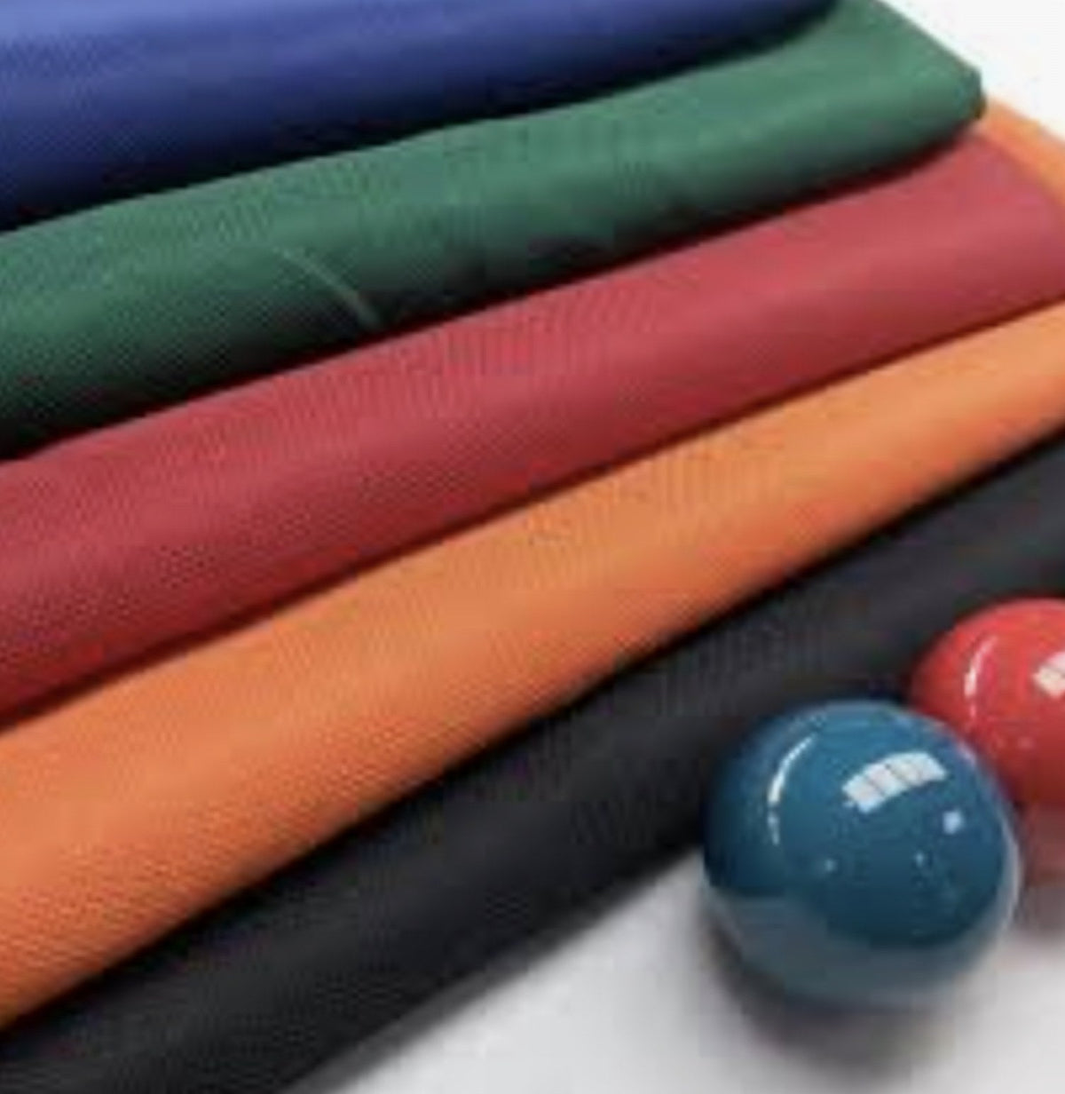 Stack of folded pool table cloth in blue, green, red, orange and black with two billiard balls