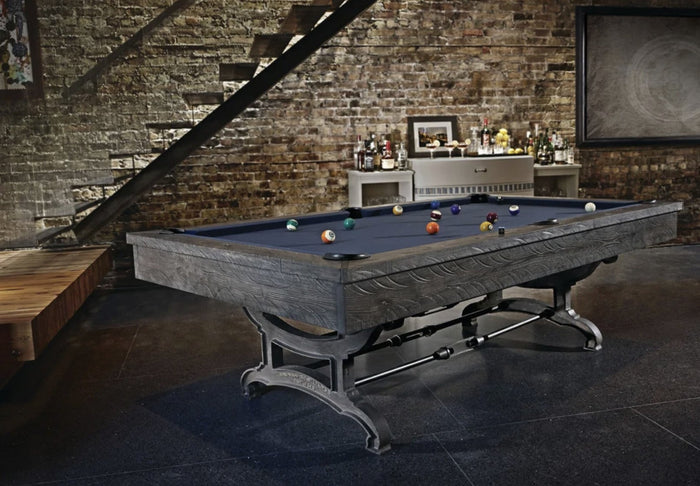 Rustic pool table in distressed gray wood with blue cloth and cast-iron legs in an exposed-brick game room